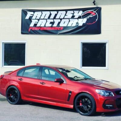 Photograph of a Chevy SS parked in front of the shop, with the shop's banner logo prominently displayed on the building in the background, setting the scene for a car enthusiast's ideal shopping destination.